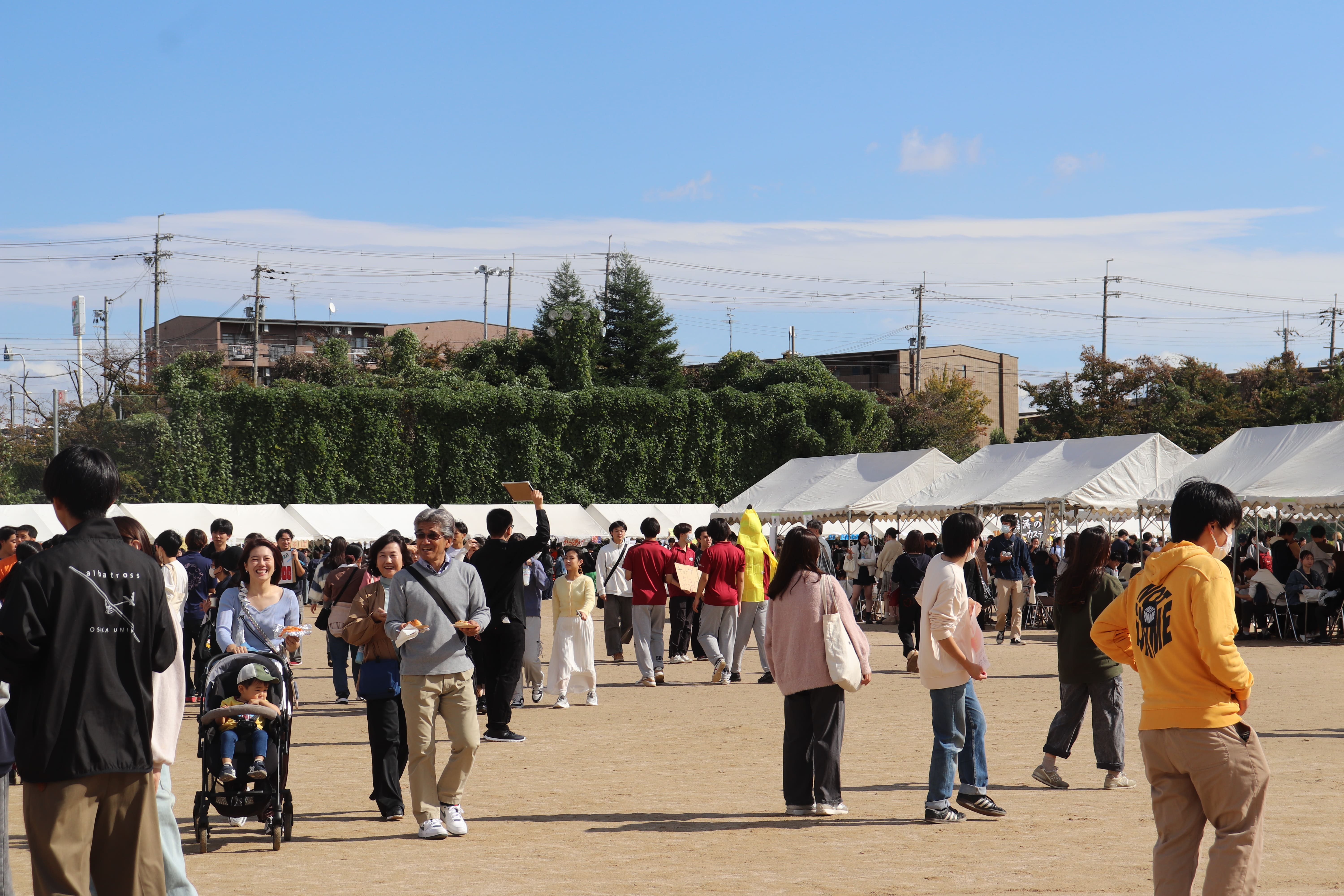 グラウンドに模擬店のテントが並び、多くの来場者で賑わっている写真