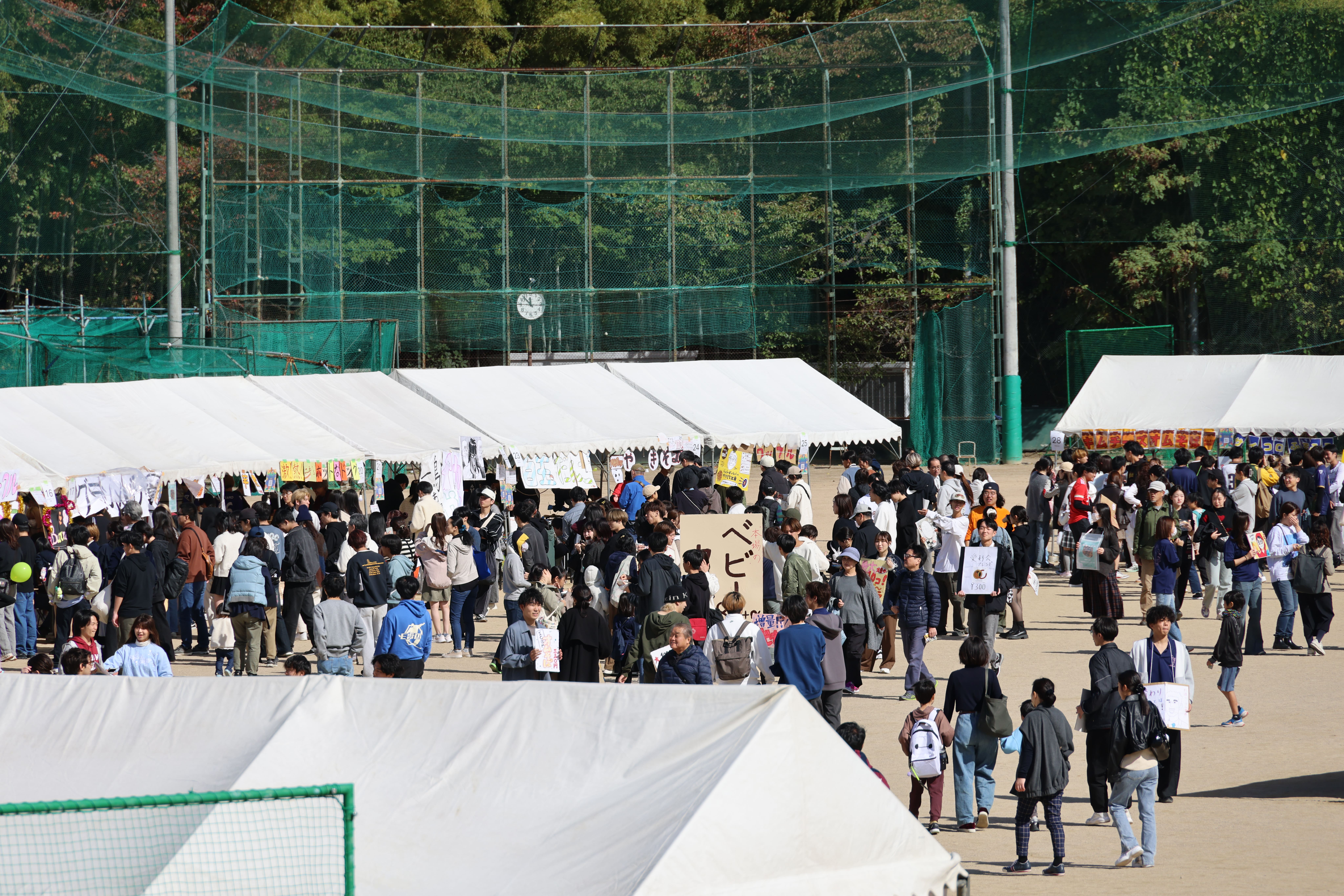 グラウンドに模擬店のテントが並び、多くの来場者で賑わっている写真